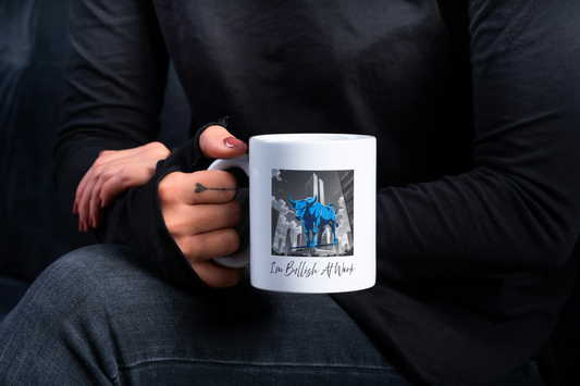 A person holding a white coffee mug with  bull bull design and text that reads I'm Bullish At Work.